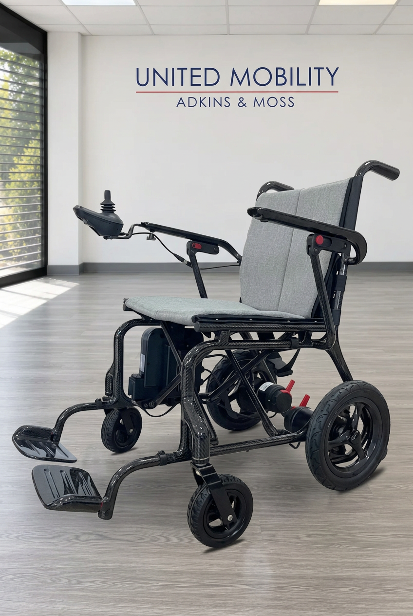 Ultralight Carbon Power Chair with grey upholstery, black folding frame, joystick and separate footplates in the United Mobility showroom.