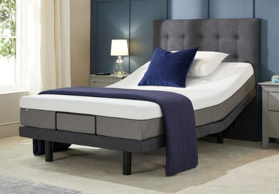 Adjustable bed with a grey upholstered headboard, blue throw, and bedside lamp.