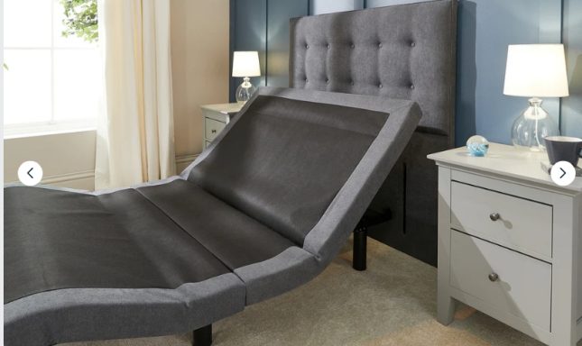 Adjustable bed with grey headboard and bedside tables in a softly lit room.