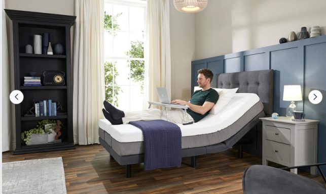 A person using a laptop while relaxing on an adjustable bed in a modern bedroom.