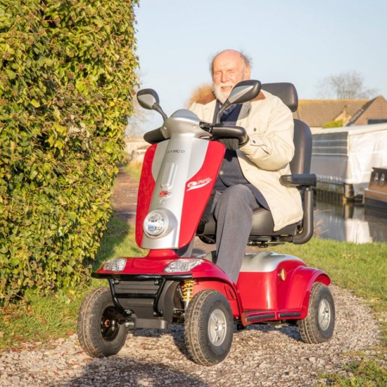 An elderly man in a scooter rides along a pathway beside a canal.